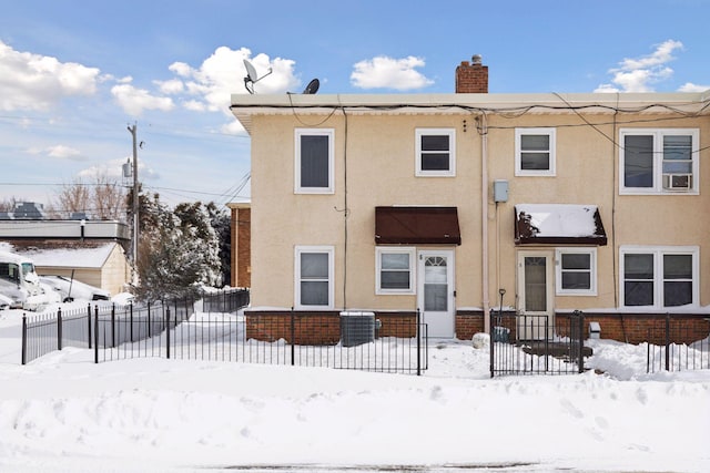 snow covered property with stucco siding, a fenced front yard, and a chimney