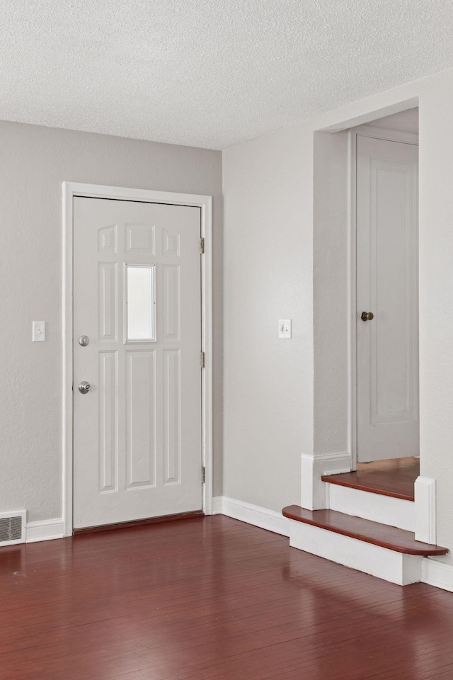 foyer featuring visible vents, baseboards, dark wood-type flooring, and a textured ceiling