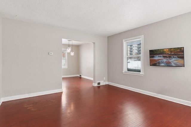 spare room with visible vents, baseboards, a textured ceiling, and dark wood-style floors