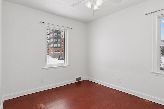 spare room with visible vents, plenty of natural light, dark wood-type flooring, and baseboards