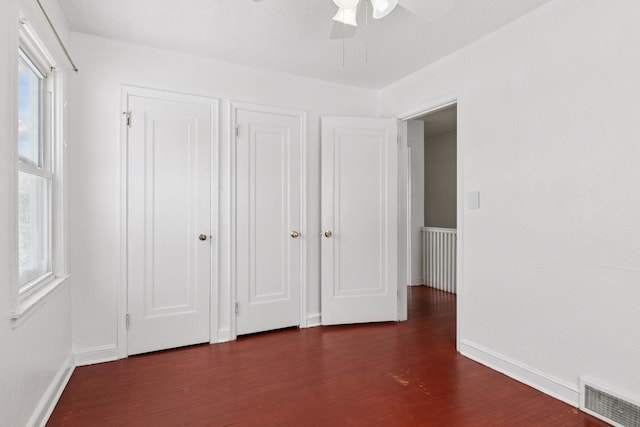 unfurnished bedroom featuring dark wood finished floors, multiple windows, baseboards, and visible vents