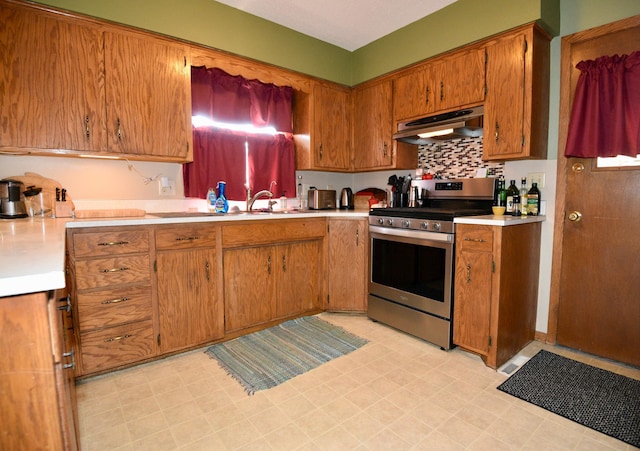 kitchen featuring brown cabinetry, stainless steel electric range, a sink, light countertops, and under cabinet range hood