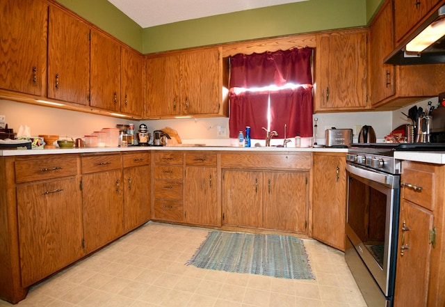 kitchen featuring brown cabinetry, stainless steel electric stove, a sink, light countertops, and under cabinet range hood