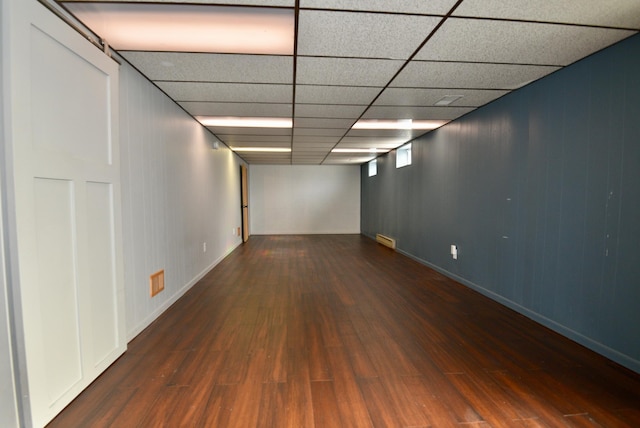 finished below grade area featuring a drop ceiling, baseboards, visible vents, and wood finished floors