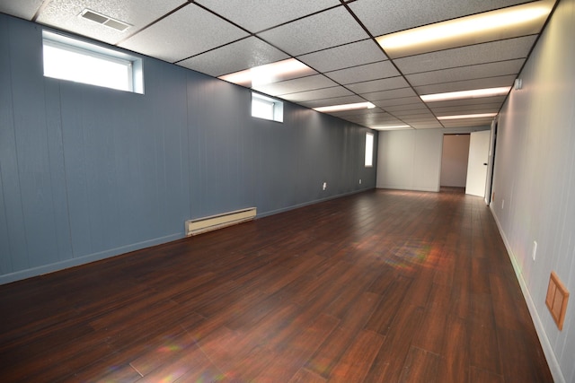 below grade area featuring baseboards, visible vents, a baseboard radiator, dark wood finished floors, and a drop ceiling