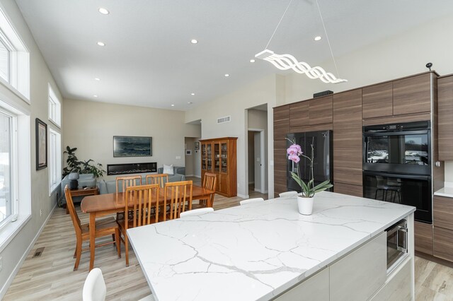 kitchen with light stone counters, light wood finished floors, recessed lighting, modern cabinets, and black appliances