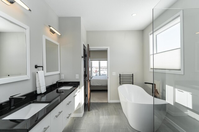 bathroom featuring double vanity, a soaking tub, a sink, and ensuite bathroom