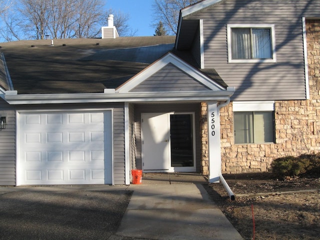 entrance to property with stone siding, a chimney, and an attached garage