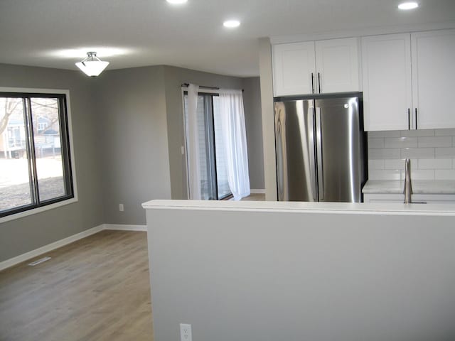 kitchen with tasteful backsplash, freestanding refrigerator, white cabinets, light wood-type flooring, and baseboards