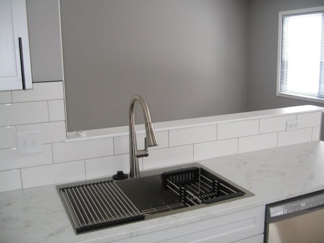 details with light stone counters, decorative backsplash, stainless steel dishwasher, white cabinets, and a sink