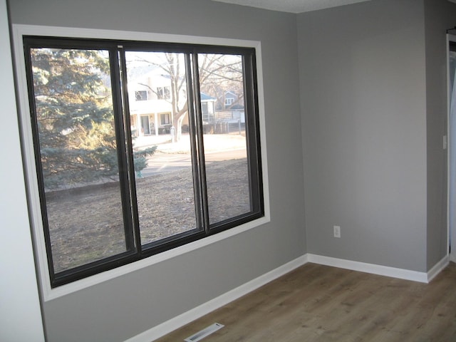 empty room with wood finished floors, visible vents, and baseboards