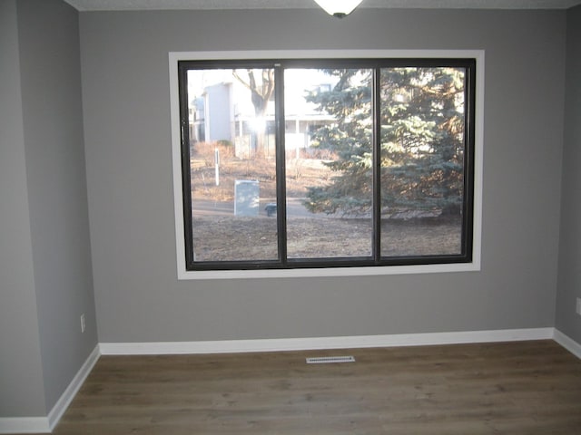 spare room featuring a healthy amount of sunlight, visible vents, and wood finished floors