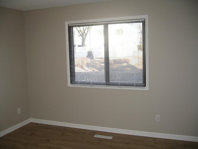 empty room with visible vents, dark wood finished floors, and baseboards