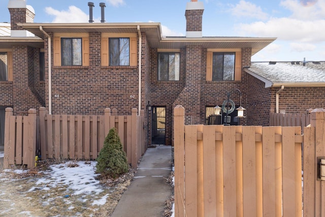 view of front of house featuring brick siding, fence, and a chimney