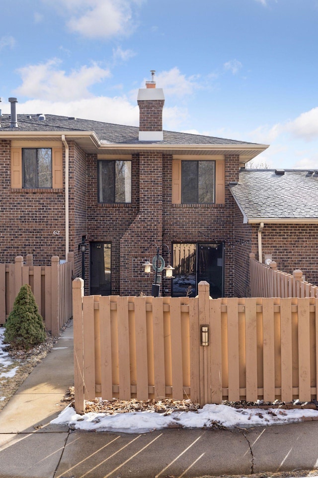 view of front of home with a fenced front yard, a chimney, roof with shingles, and brick siding