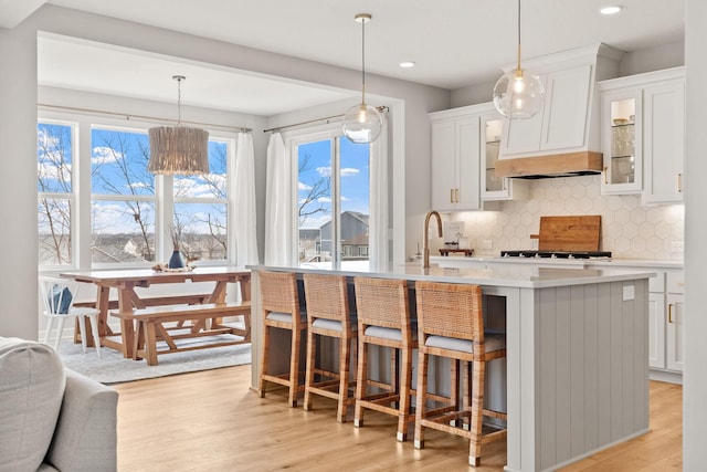 kitchen with light wood-type flooring, light countertops, a kitchen island with sink, and backsplash