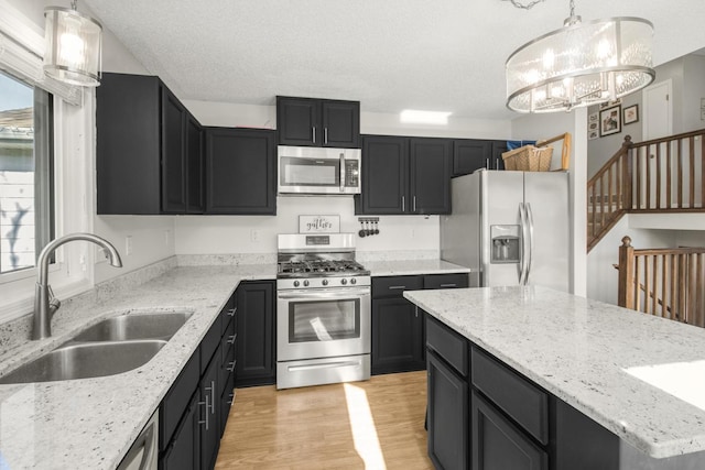 kitchen featuring light wood-style flooring, a sink, dark cabinetry, appliances with stainless steel finishes, and a chandelier