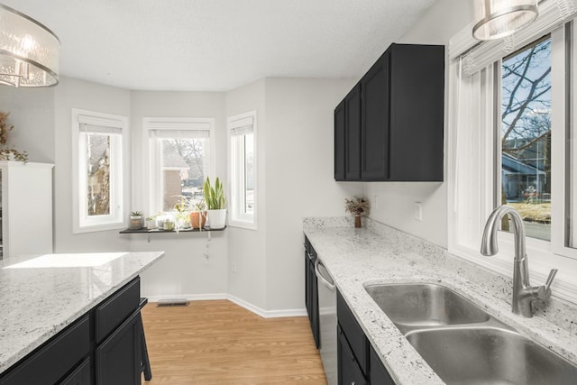 kitchen with dark cabinets, light wood-style flooring, stainless steel dishwasher, and a sink