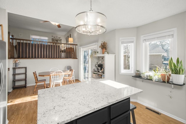 kitchen featuring light wood-type flooring, visible vents, light stone counters, dark cabinetry, and baseboards