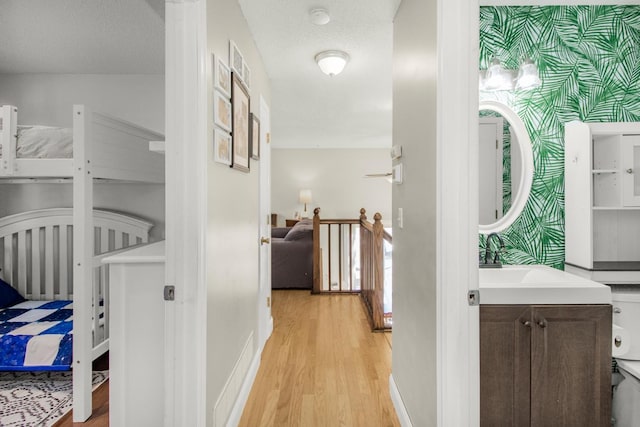 hall with light wood-type flooring, an upstairs landing, a sink, wallpapered walls, and baseboards