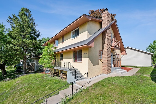 view of front of house featuring a front lawn, a chimney, a balcony, and stucco siding