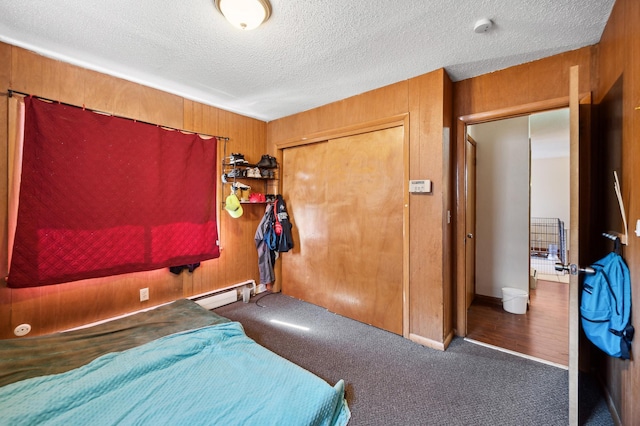 bedroom with a baseboard radiator, a textured ceiling, carpet floors, wood walls, and a closet