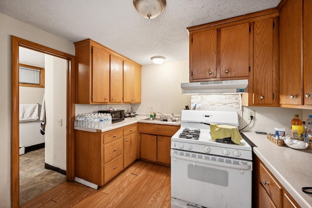 kitchen with light countertops, light wood-style flooring, a sink, under cabinet range hood, and white gas range oven