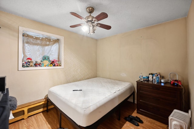 bedroom with a textured ceiling, radiator heating unit, and wood finished floors