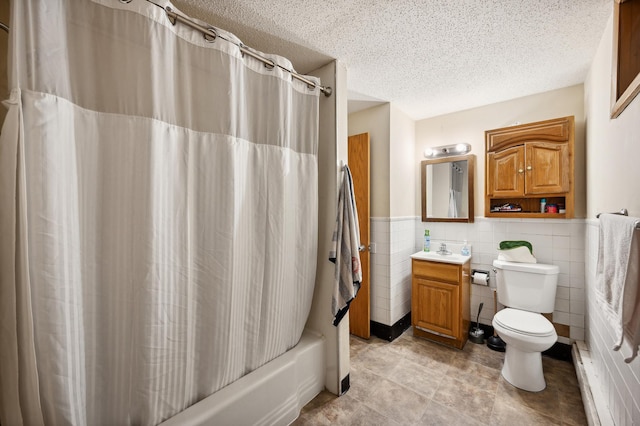 full bath featuring toilet, a wainscoted wall, a textured ceiling, vanity, and tile walls