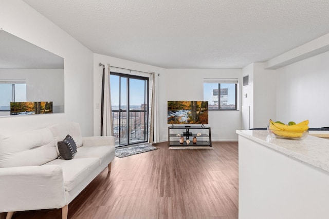 living room featuring visible vents, baseboards, a textured ceiling, and wood finished floors