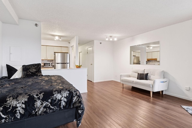 bedroom with baseboards, freestanding refrigerator, wood finished floors, a textured ceiling, and fridge