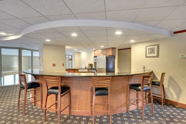 kitchen with dark countertops, a kitchen bar, carpet floors, a peninsula, and freestanding refrigerator