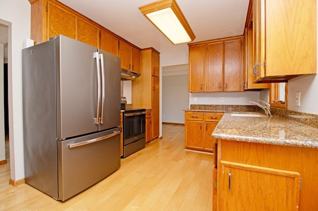 kitchen featuring stainless steel appliances, brown cabinetry, a sink, light wood-type flooring, and under cabinet range hood