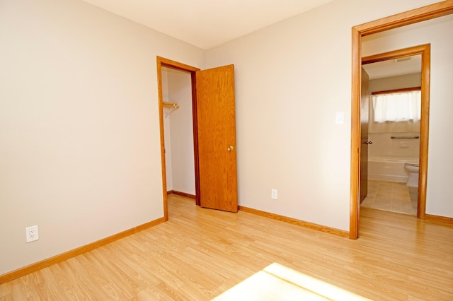 unfurnished bedroom featuring connected bathroom, baseboards, and wood finished floors