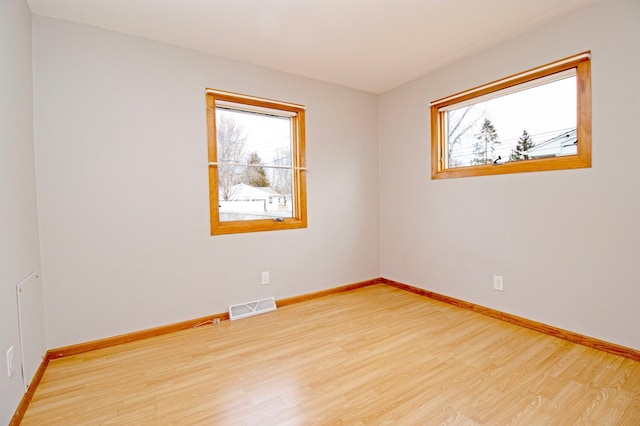 spare room featuring baseboards, light wood-style flooring, visible vents, and a wealth of natural light