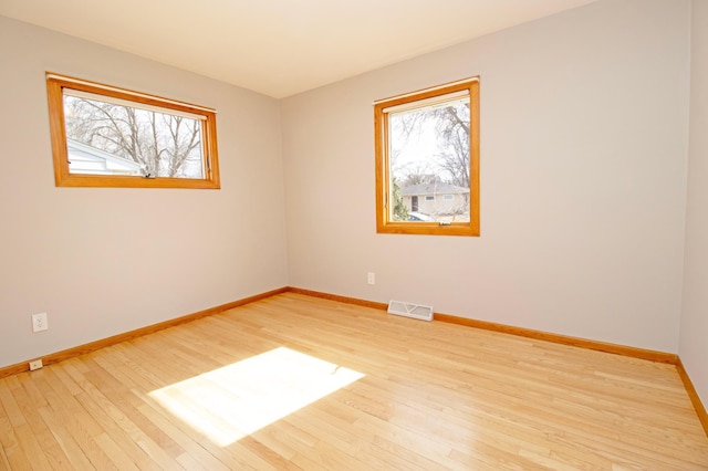 spare room featuring wood finished floors, visible vents, and baseboards