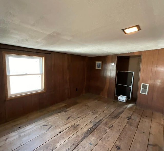 unfurnished room featuring wooden walls, light wood-type flooring, and visible vents