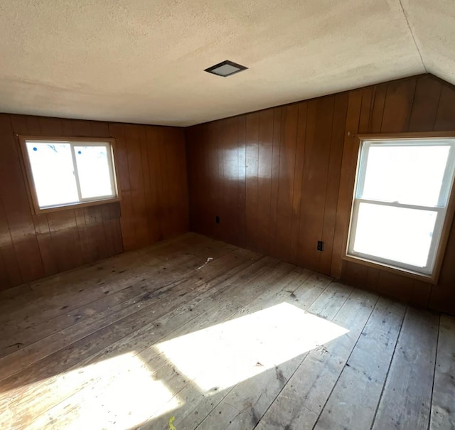 empty room featuring wooden walls, a textured ceiling, lofted ceiling, and wood-type flooring