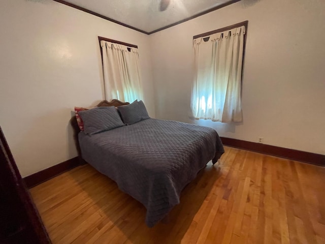 bedroom featuring ceiling fan, ornamental molding, light wood-style flooring, and baseboards