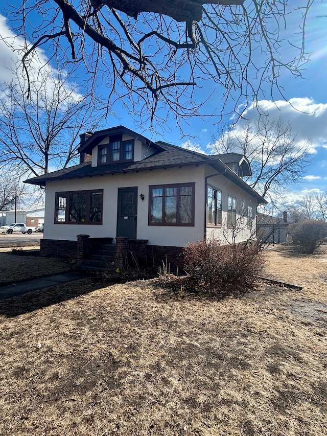 bungalow-style home featuring roof with shingles, a chimney, and stucco siding