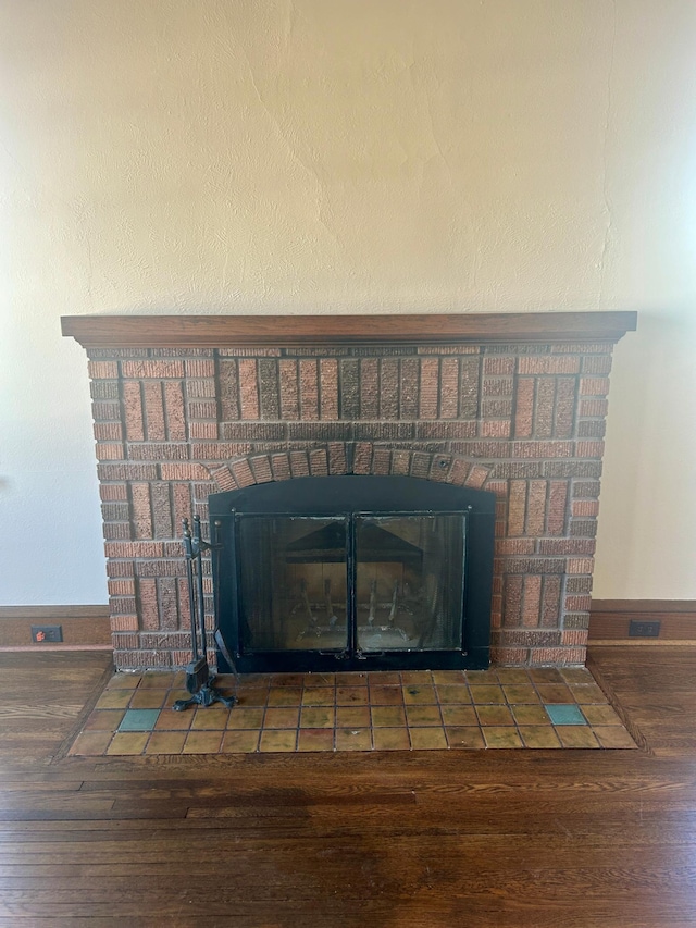 room details featuring a brick fireplace, baseboards, and wood finished floors