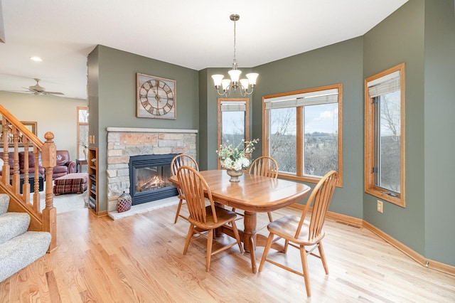 dining space with a stone fireplace, baseboards, stairway, and light wood finished floors