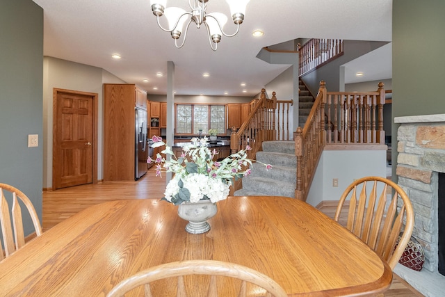 dining area with recessed lighting, a notable chandelier, a fireplace, light wood-style floors, and stairway