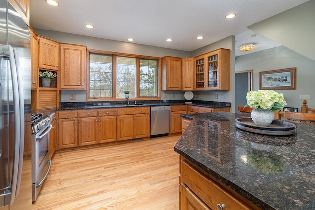 kitchen featuring dark stone counters, stainless steel appliances, light wood-style floors, a sink, and recessed lighting