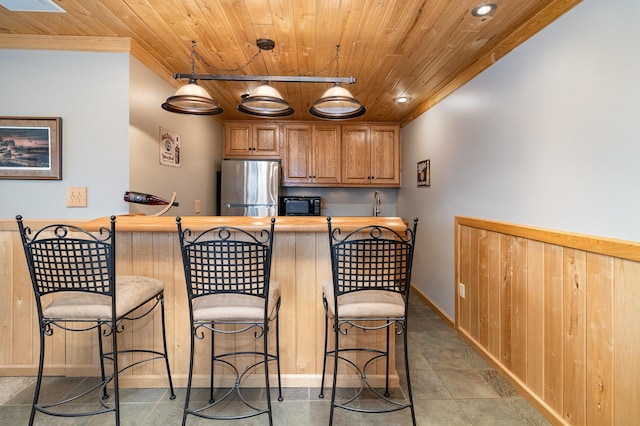 kitchen with wood ceiling, black microwave, a breakfast bar, and freestanding refrigerator