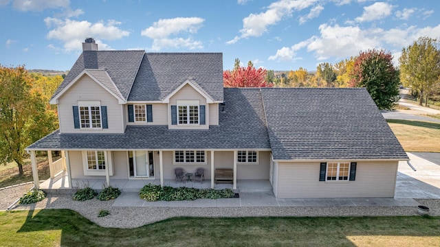 view of front of property featuring a front yard, a chimney, a porch, and roof with shingles