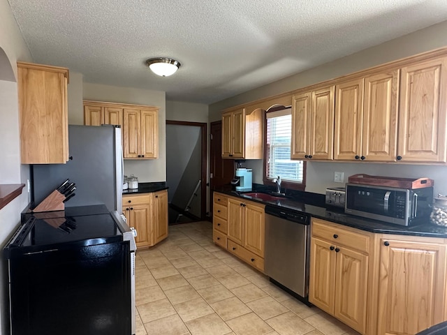 kitchen with dark countertops, light tile patterned floors, appliances with stainless steel finishes, a textured ceiling, and a sink