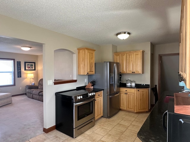 kitchen with dark countertops, a textured ceiling, open floor plan, appliances with stainless steel finishes, and light tile patterned flooring