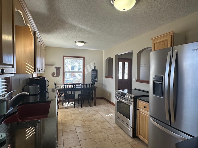 kitchen with light tile patterned floors, arched walkways, a sink, stainless steel appliances, and dark countertops