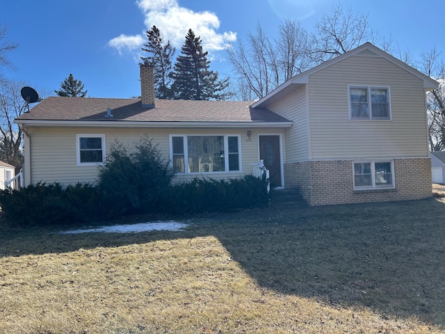 split level home with brick siding, a chimney, and a front yard